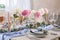 Beautiful table setting. Plate with greeting card, napkin and branch near glasses, peonies, burning candles and cutlery on table
