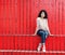 Beautiful tall girl with long hair brunette in jeans sits near wall of red wooden planks