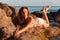 A beautiful tanned woman in her underwear lies on the coastal rocks. The sea in the background. Sunset