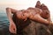 Beautiful tanned woman posing lying on her back on the coastal rocks. The sea in the background