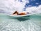 Beautiful tanned young woman lay down and relax on a trendy inflatable lilo in a paradise beach with sand and clear blue water -