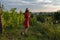 Beautiful teen girl in red dress and hat leaned on the rakes, resting while working in the vineyard, people and garden