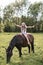 Beautiful teenage girl with long hair abd boho accessories riding horse at the field in summer. Horse riding, childhood