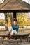 Beautiful teenage girl sitting on the park bench with black hat blue sweater and ripped jeans with blurred autumn leaves in the ba