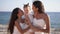 Beautiful teenage girls kissing infant standing in sunlight on sea coast. Portrait of happy Caucasian sisters enjoying