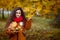 Beautiful teenager daughter in an orange jacket with luxurious hair holds a bouquet of maple leaves and looks at the branches.