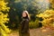 Beautiful teenager in fall park. Cheerful autumn teen with long healthy hair holding yellow maple leaf outdoors in sunny