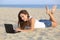 Beautiful teenager girl browsing her netbook computer lying on the sand of the beach