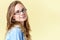 Beautiful teenager girl with ginger hair and freckles wearing reading glasses, smiling girl on yellow background