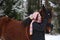 Beautiful teenager girl hugging brown horse in winter