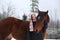 Beautiful teenager girl hugging brown horse in winter