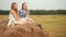 Beautiful teenager girls sitting on hay stack at harvesting field in village. Young girls posing on countryside haymow