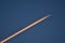 Beautiful telephoto evening view of airplane contrail in orange colors of setting Sun on dark blue background seen over Dublin