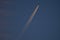 Beautiful telephoto evening view of airplane contrail in orange colors of setting Sun on dark blue background seen over Dublin