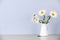 Beautiful tender chamomile flowers in jug on table against light background