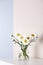 Beautiful tender chamomile flowers in vase on white wooden commode near color wall