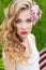 Beautiful tender sweet girl in a white dress with a wedding hairdo curls bright makeup and red lips with flowers in her hair