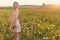 Beautiful tender sweet girl in a white lace dress with a scythe on his head standing barefoot in a field of dandelions in the sun