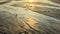Beautiful textured golden sand with streams of water at low tide on seaside. Sunset on sea shore. Natural background of