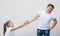 Beautiful thin little caucasian girl pulling with both hands fat strong boy in white shirt and jeans hand on bright background