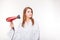 Beautiful thoughful woman in bathrobe drying her hair with dryer