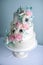 Beautiful three tiered white wedding cake decorated with flowers sugar pink peonies. Concept of elegant holiday desserts