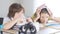 Beautiful tired schoolgirl putting book on head and looking at camera with blurred schoolboy sitting at desk at front