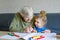 Beautiful toddler girl and grand grandmother drawing together pictures with felt pens at home. Cute child and senior