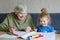 Beautiful toddler girl and grand grandmother drawing together pictures with felt pens at home. Cute child and senior