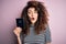 Beautiful tourist woman with curly hair and piercing holding australia australian passport id scared in shock with a surprise