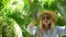 Beautiful traveler woman with hat smiling behind palm trees. Sunlight. Concept travel, vacation