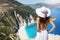 A beautiful traveler woman in white dress looks at the famous beach of Myrtos, Kefalonia, Greece