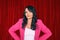 Beautiful trendy actress woman entertainer in pink suit on red velvet curtains background.