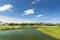 Beautiful tropical natural landscape view. Green grass field and pond water surface on blue sky with rare white clouds background