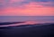 Beautiful twilight dramatic purple sky over the sea with colourful evening clouds reflected in calm water and dark beach