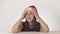 Beautiful unhappy girl teenager in a Santa Claus hat emotionally expresses despair and begins to cry on white background