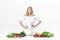 Beautiful upset blond woman in white clothes and lots of fresh vegetables on white background. diet