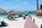 Beautiful view of coast line. Tourists on blue sun beds, white sand and palm trees on blue sky background. Eagle Beach.