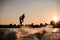 beautiful view of dark silhouette of active male rider holds rope and making extreme jump on wakeboard at sunset.