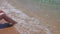 Beautiful view of female sitting on sand beach with legs in oncoming wave.