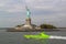 Beautiful view of green speedboat passing by famous Statue of Liberty.