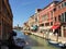 A beautiful view looking down a busy canal in Murano, Italy.  Boats are driving down the canal and tourists are visiting the shops