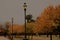 Beautiful view of a park with autumnal trees and tall lamp posts under the cloudy sky