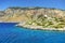 Beautiful view on Symi island stone rocks white mill flouring-mill with orange roof on green hill. Blue crystal clear water of Aeg