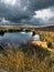 Beautiful view of thick gloomy clouds reflected on the surface of the pond surrounded by dry grass