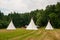 Beautiful view of three tipi tents in a field. Tee pee built on green grass. Traditional teepee tent wigwams located in nature.