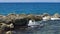 Beautiful view of waves breaking on stones. Turquoise water of Atlantic ocean and big rocks on blue sky background.