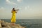 Beautiful violinist girl in yellow concert dress is playing electric violin on rocks by the Mediterranean sea in Antalya, Turkey.