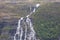 Beautiful waterfall flowing down a massive structured steep stone wall with green grass and moss in the mountains on the Lofoten