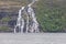 Beautiful waterfall flowing down a massive structured steep stone wall with green grass and moss in the mountains on the Lofoten